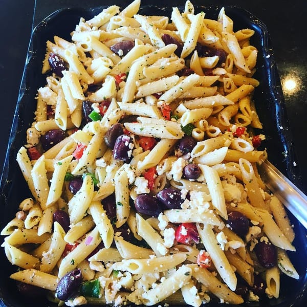 A large tray of Cogman's Creek pasta salad with penne, olives, feta, and red peppers.