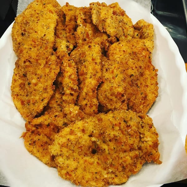 Golden-brown breaded chicken cutlets, likely from Cogman’s Creek, piled high on white parchment paper.