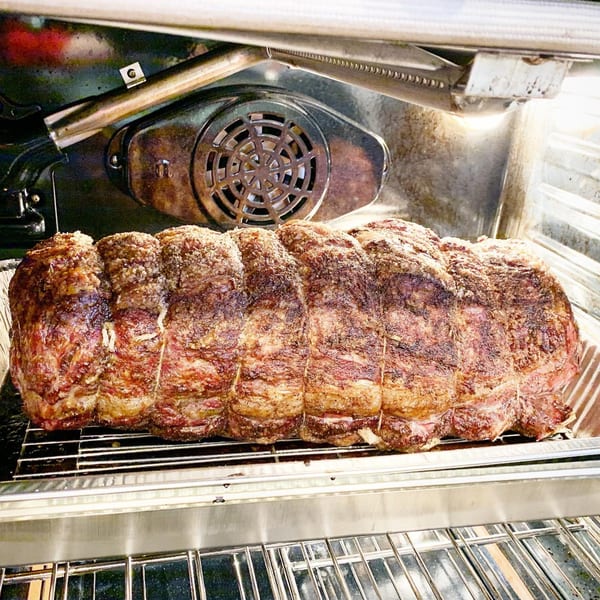 A large, seasoned roast cooking in an oven, tied with butcher's twine.