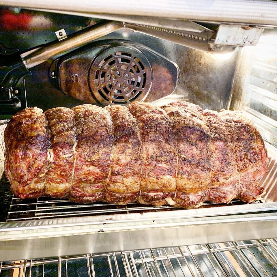 A large, seasoned roast cooking in an oven, tied with butcher's twine.