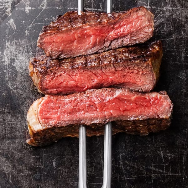 Three perfectly cooked, medium-rare Cogman's Creek steaks on a dark, textured surface.