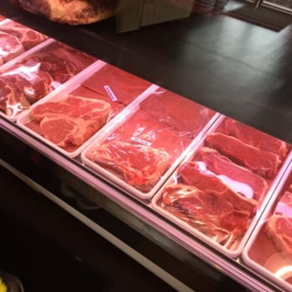 Various cuts of fresh red meat, including steaks, displayed in a refrigerated butcher shop case.