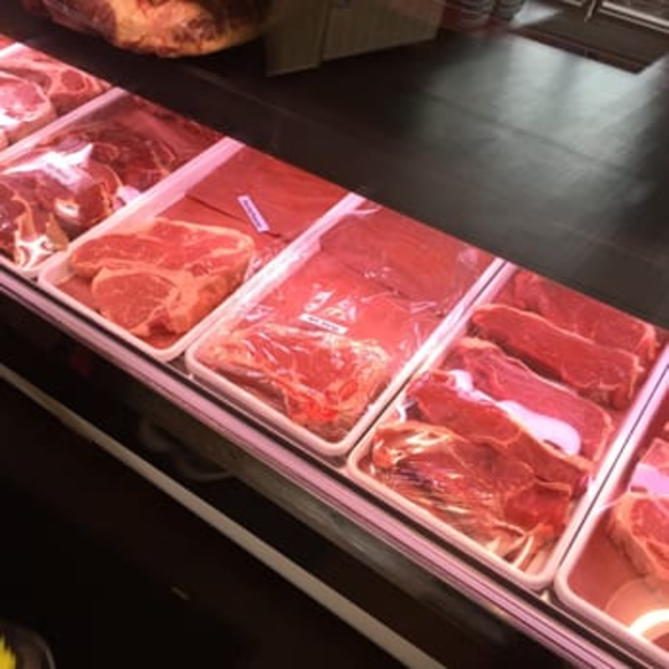 Various cuts of fresh red meat, including steaks, displayed in a refrigerated butcher shop case.